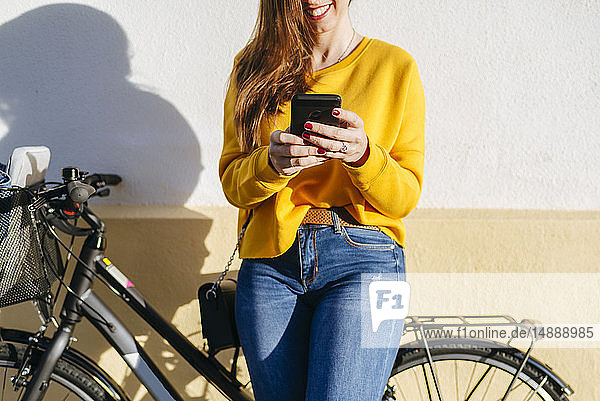 Nahaufnahme einer jungen Frau mit Fahrrad  die mit ihrem Handy an einer Wand telefoniert