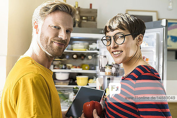 Porträt eines Paares mit Tablette vor dem Kühlschrank beim Online-Einkauf von Lebensmitteln