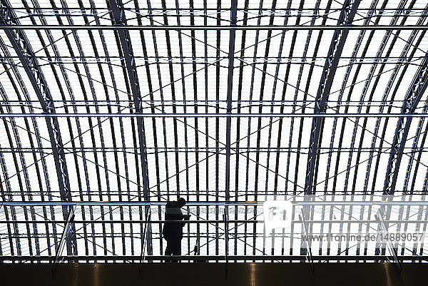 Silhouette eines Geschäftsmannes  der mit einem Mobiltelefon auf einem Bahnsteig im Bahnhof steht