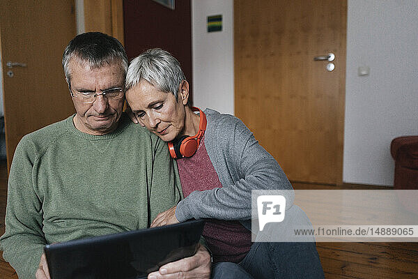 Älteres Ehepaar sitzt zu Hause auf dem Boden und schaut auf die Tablette