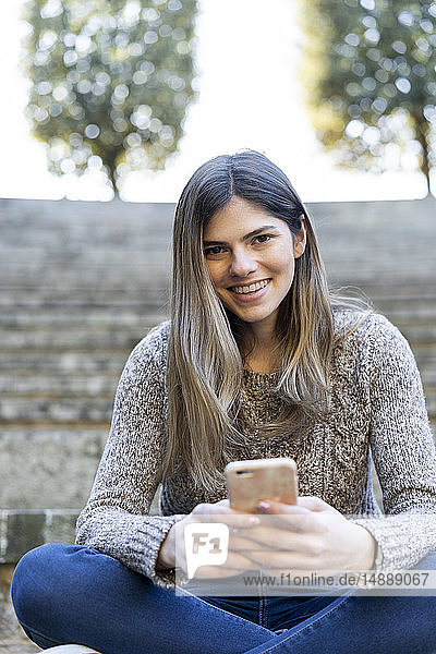 Porträt einer glücklichen jungen Frau mit Handy in der Hand