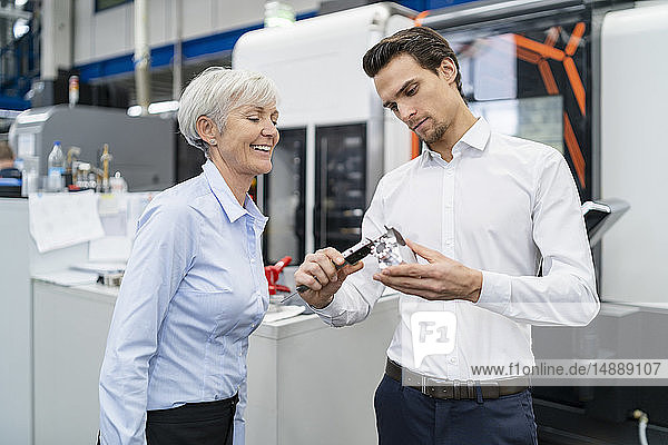 Businessman and senior businesswoman measuring workpiece in a factory
