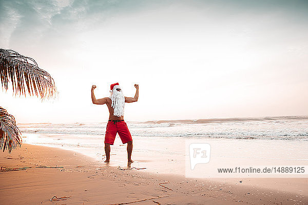 Thailand  als Weihnachtsmann verkleideter Mann posiert bei Sonnenuntergang am Strand