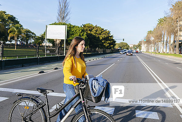 Junge Frau mit Fahrrad beim Überqueren der Straße