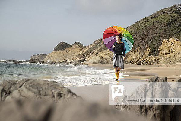 Woman with colorful umbrella walking on the beach