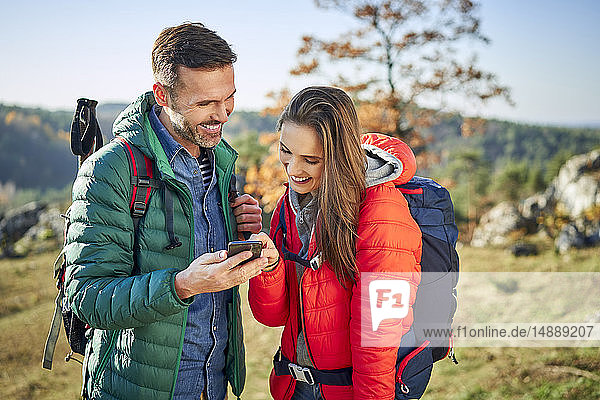 Happy couple on a hiking trip in the mountains checking cell phone