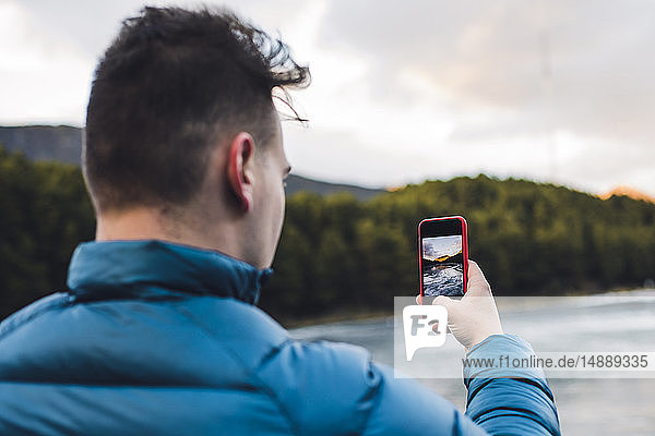 Young man taking cell phone picture at a frozen lake in winter