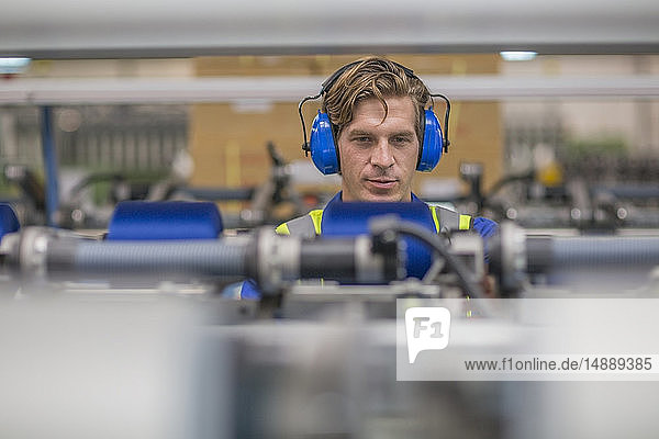 Mann trägt Gehörschützer bei der Bedienung einer Maschine in einer Fabrik