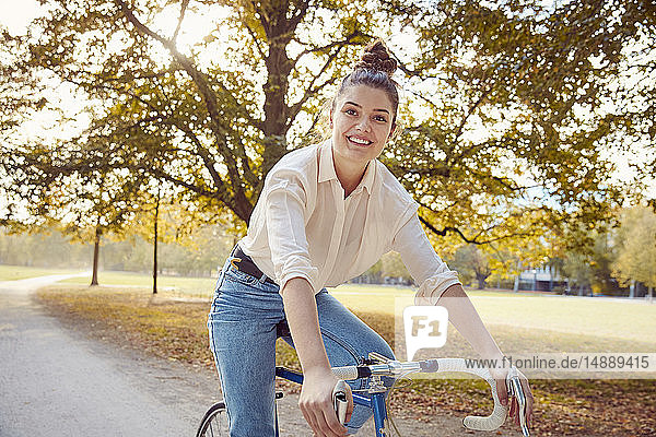 Porträt einer lächelnden jungen Frau beim Fahrradfahren in einem Park