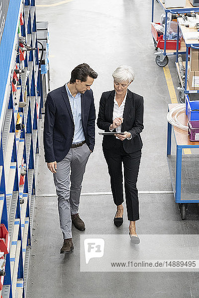 Businessman and senior businesswoman with tablet walking in a factory