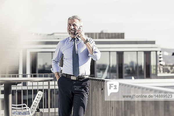 Smiling mature businessman on cell phone on roof terrace