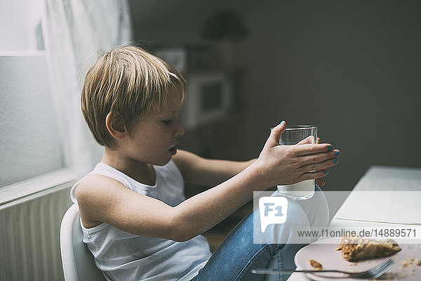 Kleiner Junge mit blauem Nagellack am Frühstückstisch sitzend mit einem Glas Milch