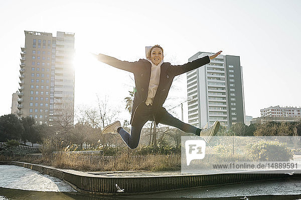 Happy young woman jumping in a park with the city in background