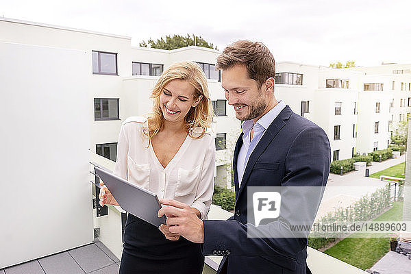 Real estate agent standing on a balcony with customer  looking at digital tablet