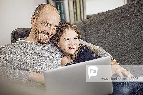 Vater und Tochter sitzen auf der Couch und benutzen einen Laptop