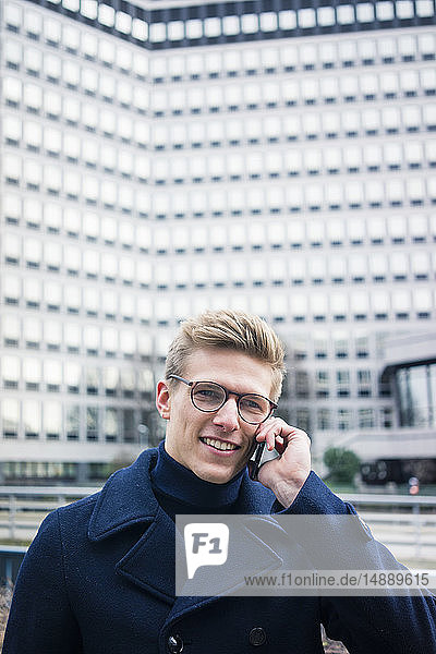 Porträt eines lächelnden jungen Mannes beim Telefonieren in der Stadt