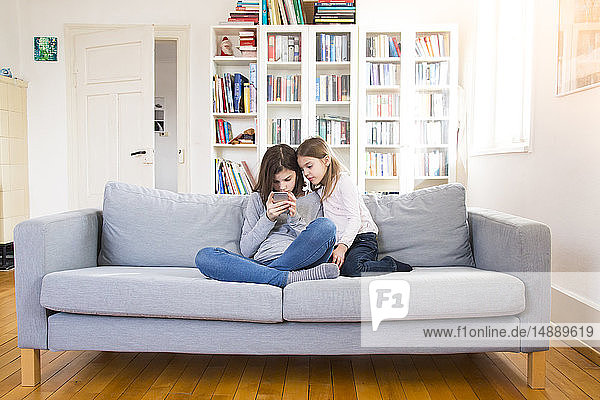 Schwestern sitzen auf der Couch und benutzen ein Mobiltelefon