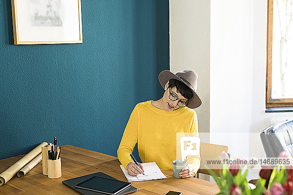 Geschäftsfrau im Home-Office schreibt auf einem Blatt Papier mit Kaffeetasse