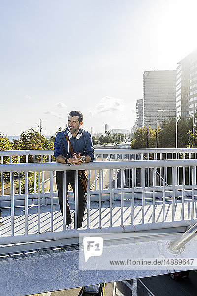 Man leaning on railing of footbridge looking at distance