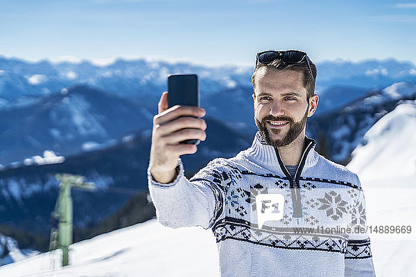 Deutschland  Bayern  Brauneck  Mann im Winter in den Bergen beim Selfie
