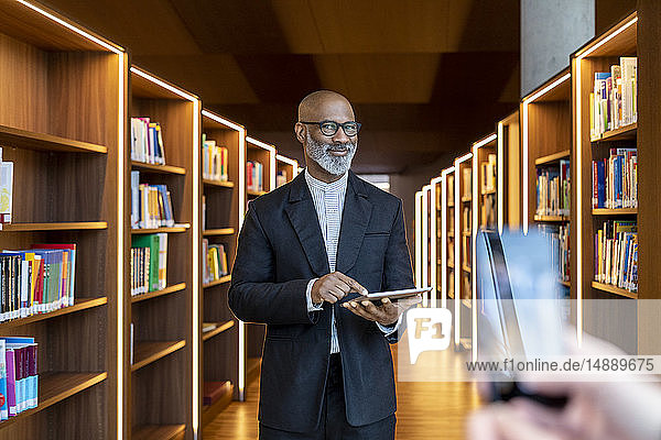 Porträt eines lächelnden Geschäftsmannes mit digitalem Tablett in der Bibliothek
