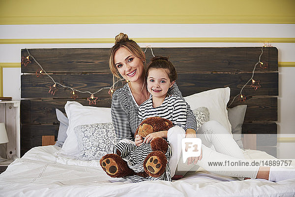 Mother and daighter sitting on bed  girl honding teddy bear