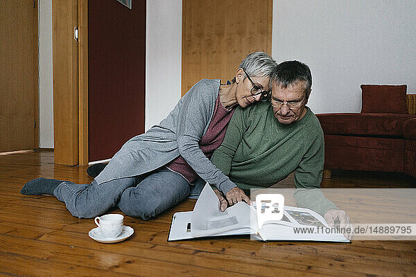 Älteres Ehepaar sitzt zu Hause auf dem Boden und schaut sich ein Fotoalbum an
