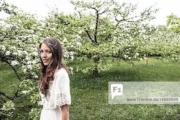 Porträt einer lächelnden jungen Frau im Garten mit blühenden Apfelbäumen