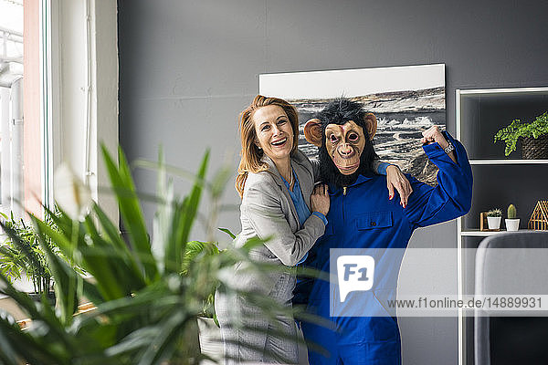Geschäftsfrau  die mit einem Auszubildenden im Amt steht  mit Affenmaske und blauer Evrall