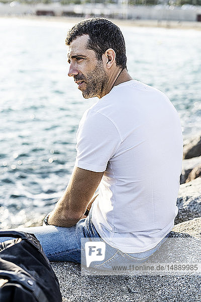 Mann sitzt auf einem Felsen vor dem Meer und entspannt
