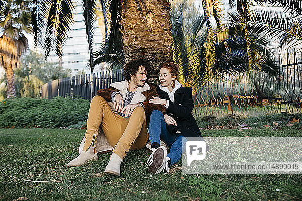 Paar  das im Park sitzt und sich an eine Palme lehnt