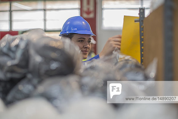 Frau mit Schutzhelm trägt Kontrolldokument in Fabrik