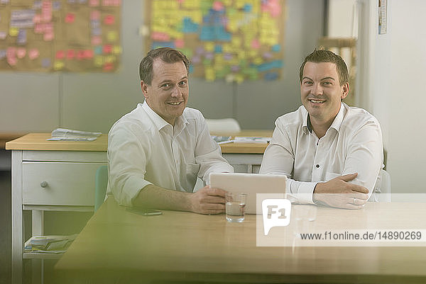 Porträt von zwei lächelnden Geschäftsleuten mit Tablett im Büro