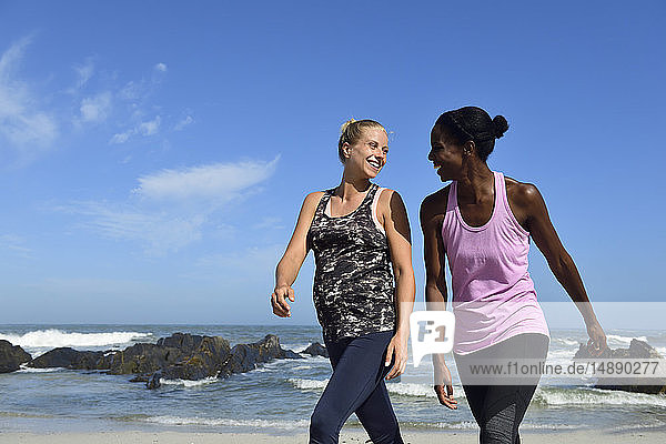 Zwei glückliche Frauen gehen am Strand spazieren