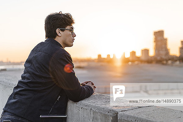 Spanien  Barcelona  Profil eines jungen Geschäftsmannes  der bei Sonnenuntergang an einer Wand lehnt und die Aussicht betrachtet