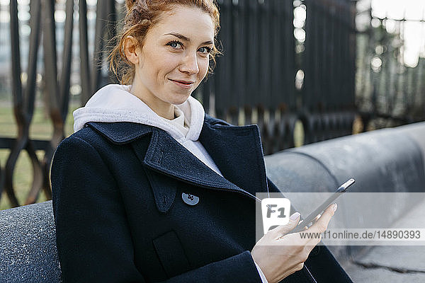 Portrait of smiling young woman sitting on a bench holding cell phone
