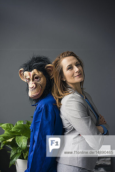 Geschäftsfrau  Rücken an Rücken mit einem Auszubildenden stehend  mit Affenmaske und blauer Evrall