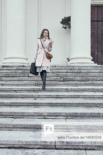 Österreich  Wien  junge Geschäftsfrau geht die Treppe hinunter und schaut auf ihr Handy
