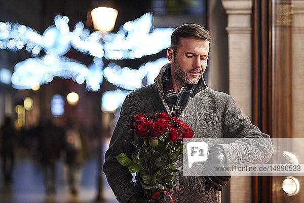 Porträt eines wartenden Mannes mit einem Strauss roter Rosen  der die Zeit kontrolliert