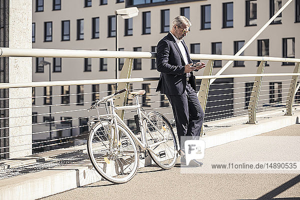 Mature businessman with bicycle using cell phone in the city