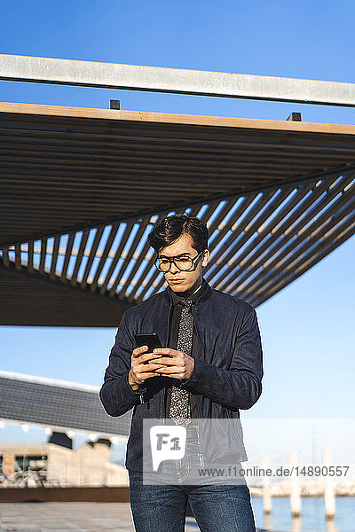 Porträt eines modischen jungen Geschäftsmannes mit Brille und Krawatte beim Blick auf sein Handy