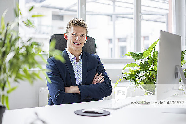 Porträt eines selbstbewussten jungen Geschäftsmannes  der im Büro am Schreibtisch sitzt
