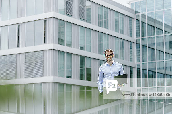 Young businessman standing in front of modern office building  using laptop