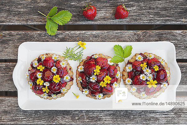 Hausgemachte Erdbeer-Herztörtchen mit Gänseblümchen und goldener Ringelblume  essbare Blüten  dunkles Holz
