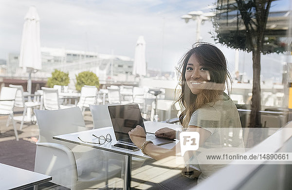 Porträt einer lächelnden Frau  die im Straßencafé sitzt und am Laptop arbeitet