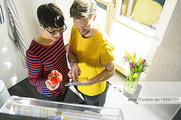 Glückliches Paar mit Tablette vor dem Kühlschrank beim Online-Einkauf von Lebensmitteln