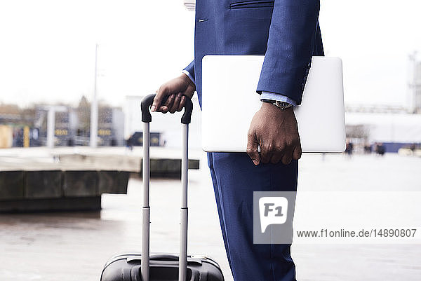 Waiting businessman with laptop and trolley bag wearing blue suit  partial view