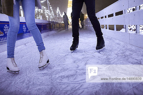 Beine eines Paares  das nachts auf einer Eisbahn eisläuft