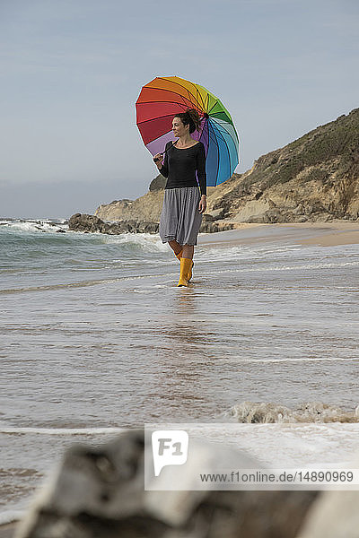 Frau mit buntem Regenschirm am Strand stehend
