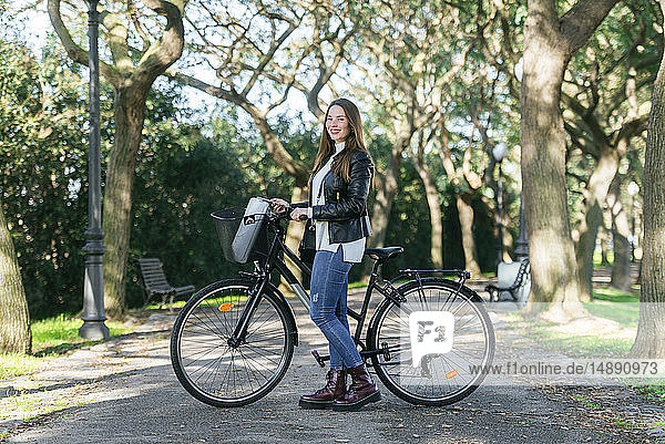 Porträt einer lächelnden jungen Frau mit Fahrrad im Park